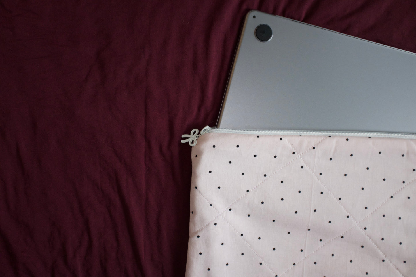 Silver laptop in a pink polka dot pouch on a maroon surface