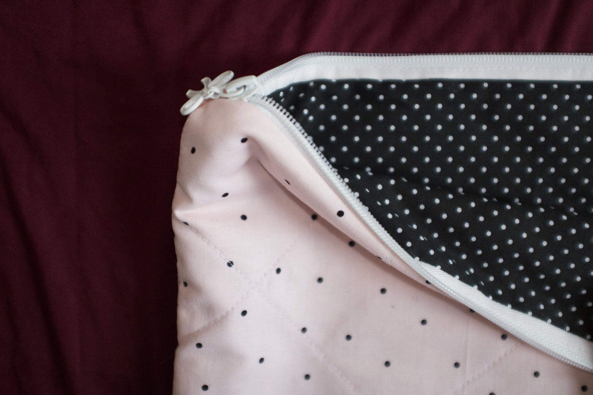 Close-up of a pink fabric with black polka dots and a zipper on a dark background