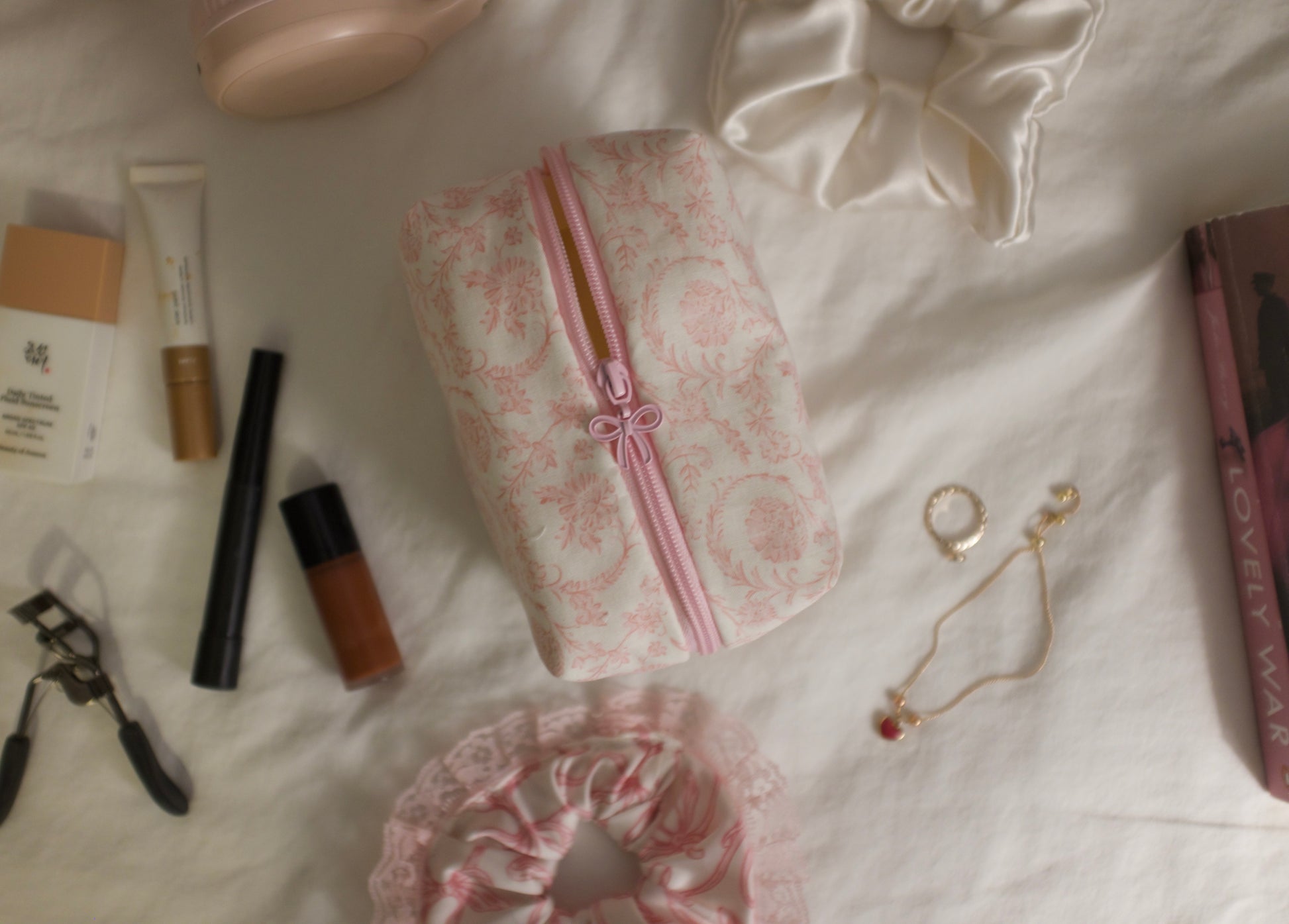 Makeup products and accessories on a white surface showcasing a pink and white floral makeup pouch 