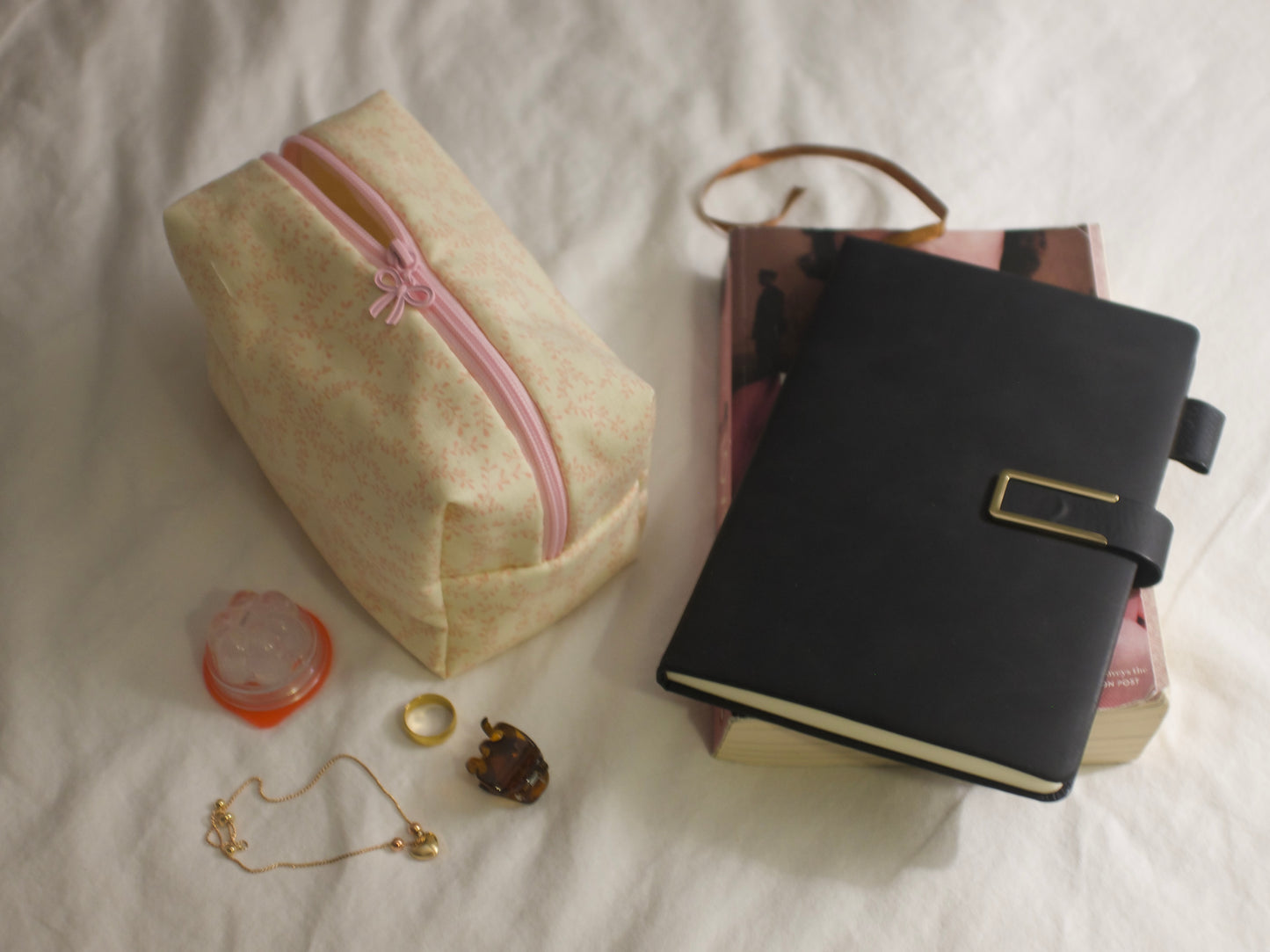 Yellow and pink floral pouch with pink zipper, black notebook, and small items on a white surface