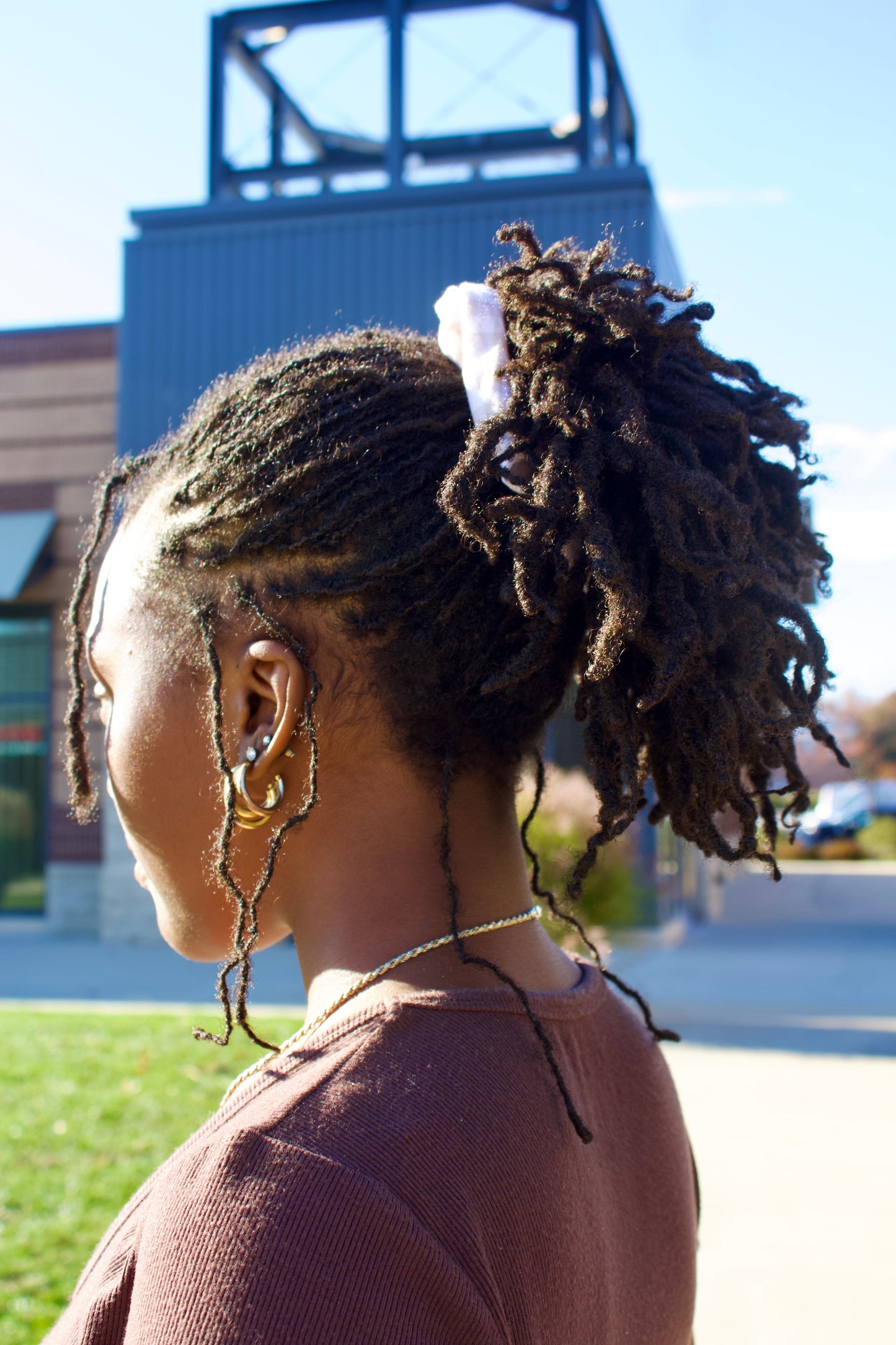 Person with styled hair outdoors, with a building and clear sky in the background